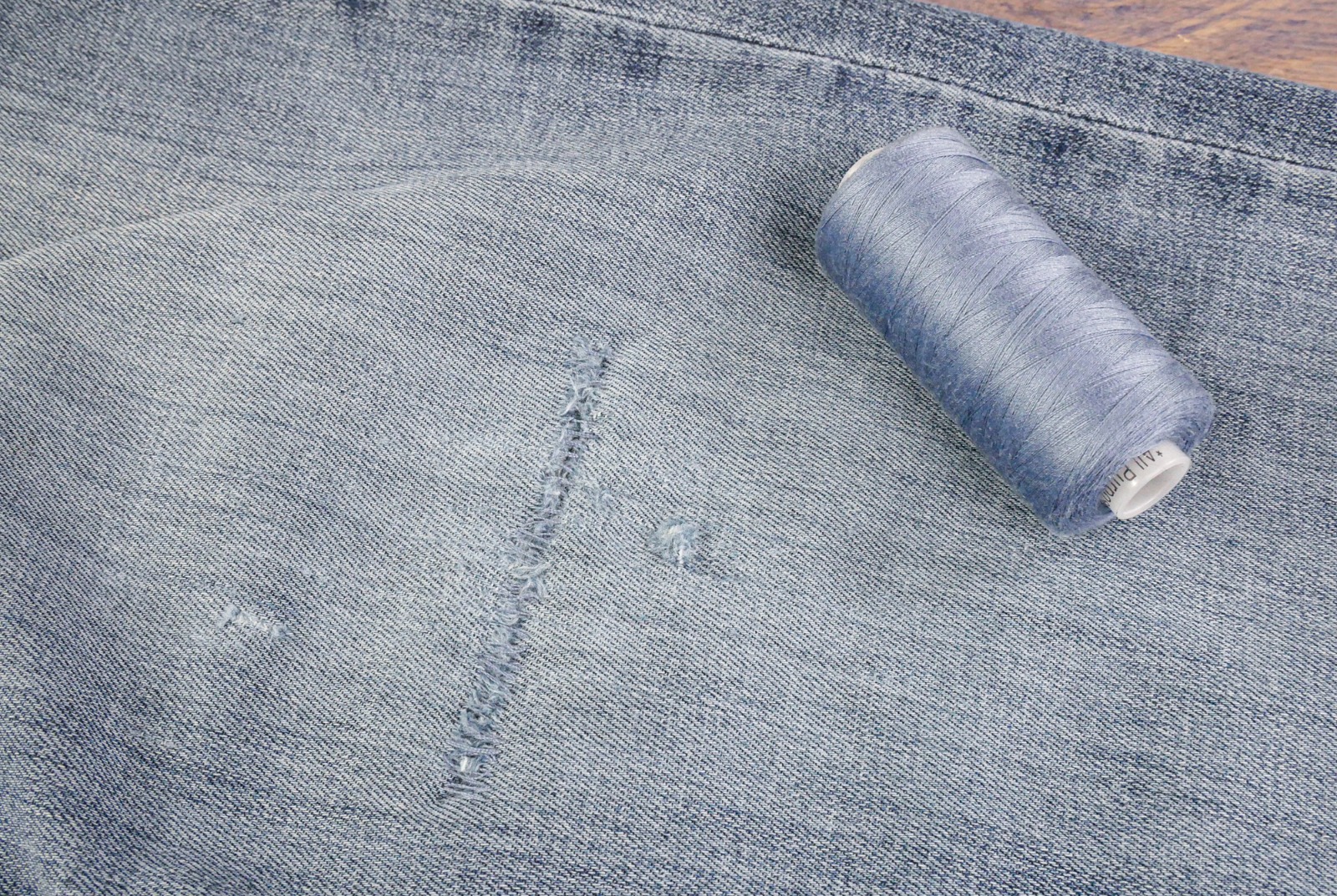 A photo of a hole in a pair of denim jeans repaired using hand sewing.